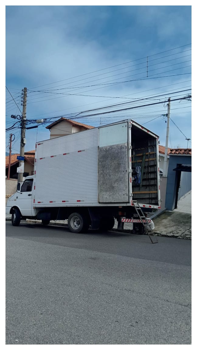 Caminhão branco estacionado em rua residencial com a rampa de acesso preparada para carga.