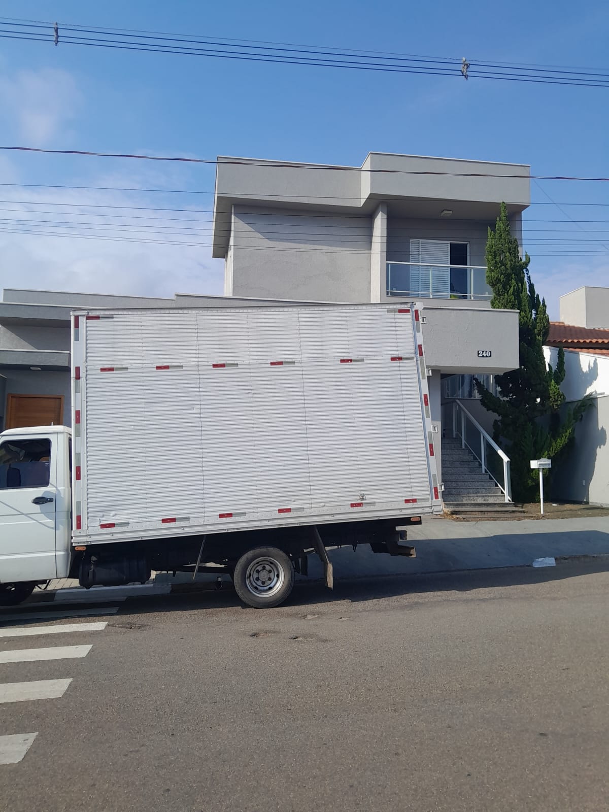 Caminhão baú branco da Airton Mudanças estacionado em frente a um prédio residencial.
